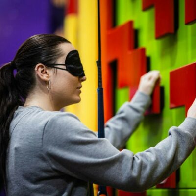 Female completing a team building challenge at High Rise Lisburn, holding on to a clip and climb wall while blindefolded.