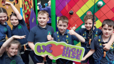 School children doing funny poses while holding a 'We love High Rise' sign in the Clip 'n Climb arena at High Rise Lisburn