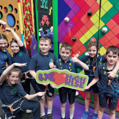 School children doing funny poses while holding a 'We love High Rise' sign in the Clip 'n Climb arena at High Rise Lisburn