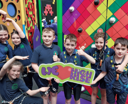 School children doing funny poses while holding a 'We love High Rise' sign in the Clip 'n Climb arena at High Rise Lisburn