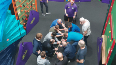 Group of adult men completing a team building challenge in the Clip 'n Climb arena at High Rise Lisburn