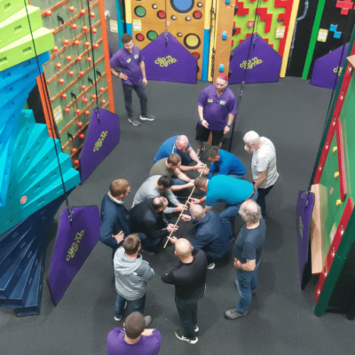 Group of adult men completing a team building challenge in the Clip 'n Climb arena at High Rise Lisburn