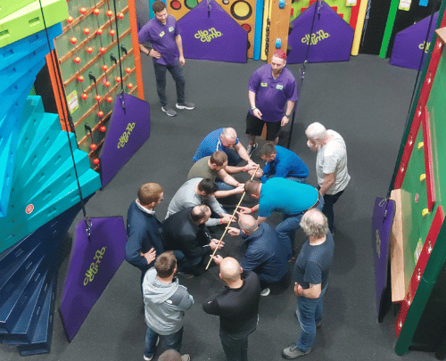 Group of adult men completing a team building challenge in the Clip 'n Climb arena at High Rise Lisburn