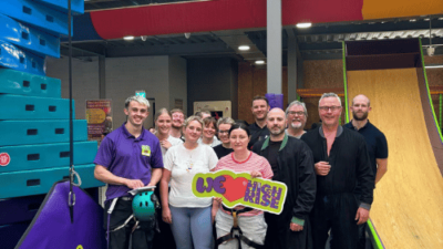 Group of adults smiling while holding a 'We love High Rise' sign in the climbing arena at High Rise Lisburn