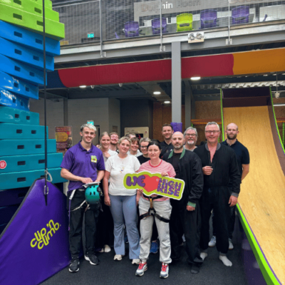 Group of adults smiling while holding a 'We love High Rise' sign in the climbing arena at High Rise Lisburn
