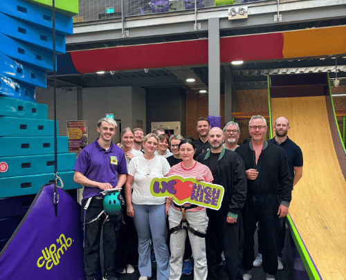 Group of adults smiling while holding a 'We love High Rise' sign in the climbing arena at High Rise Lisburn